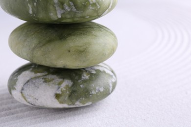 Photo of Zen garden stones on white sand with pattern, closeup. Space for text