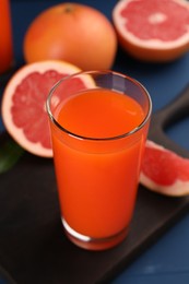 Photo of Tasty grapefruit juice in glass and fresh fruits on blue wooden table, closeup