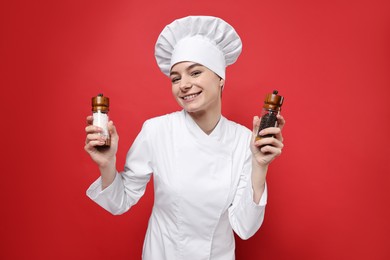 Photo of Professional chef holding salt and pepper shakers on red background