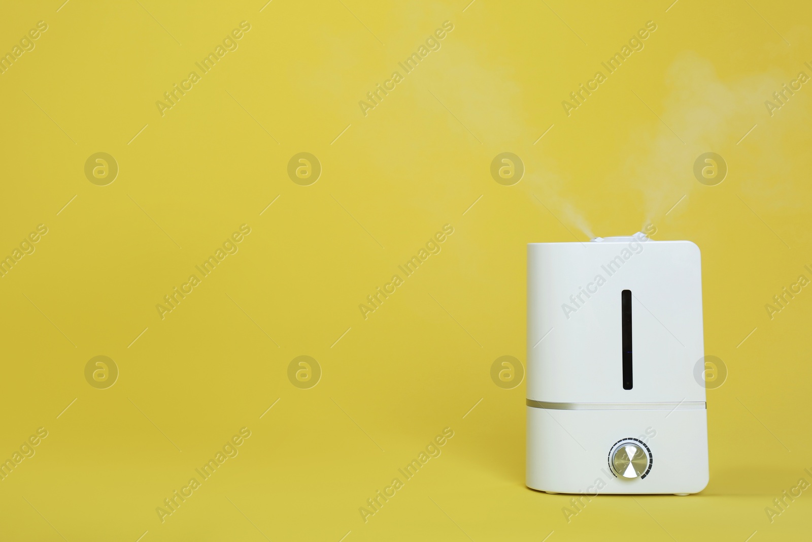 Photo of Modern air humidifier on yellow background. Space for text