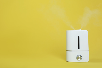 Photo of Modern air humidifier on yellow background. Space for text