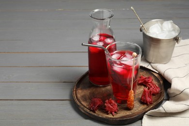 Photo of Refreshing hibiscus tea with ice cubes, stick with sugar crystals and roselle petals on grey wooden table. Space for text