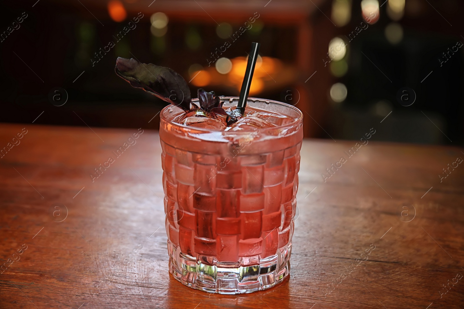 Photo of Glass with delicious cocktail and ice cubes on counter in bar