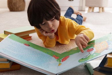 Cute little boy reading book on floor at home