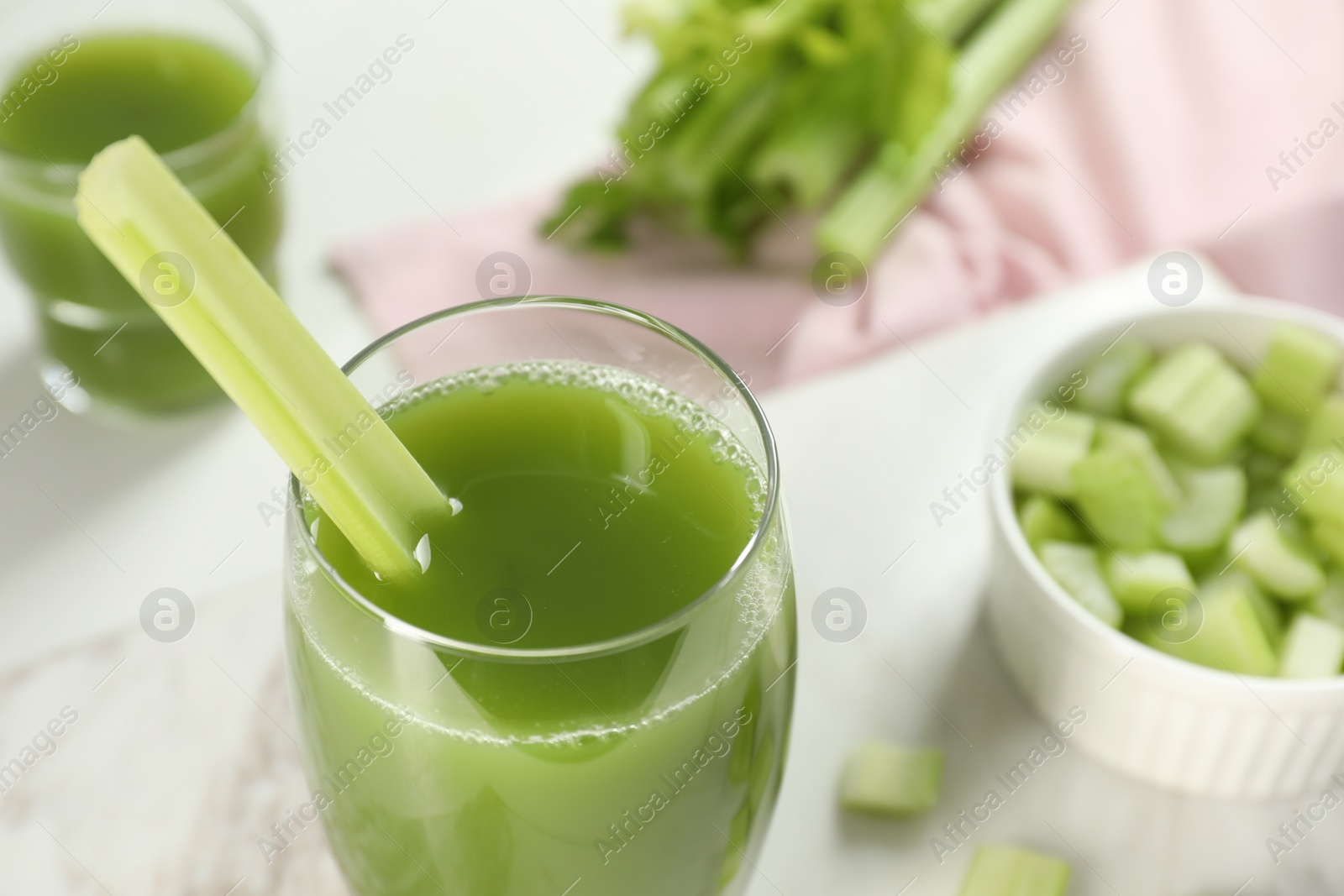 Photo of Glass of delicious celery juice and vegetables on white table, closeup