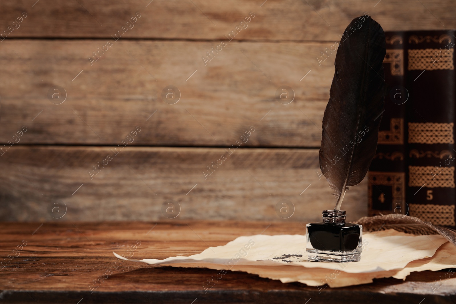 Photo of Inkwell with feather and vintage parchment with stains near books on wooden table. Space for text