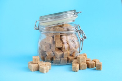 Photo of Brown sugar cubes in glass jar on light blue background