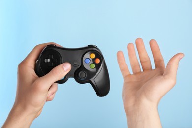 Man using wireless game controller on light blue background, closeup