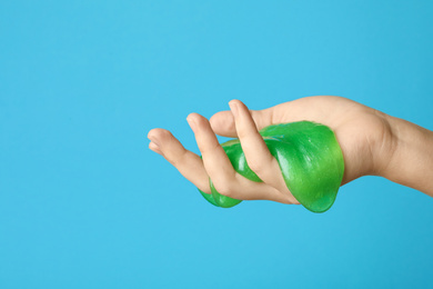 Woman playing with green slime on light blue background, closeup. Antistress toy