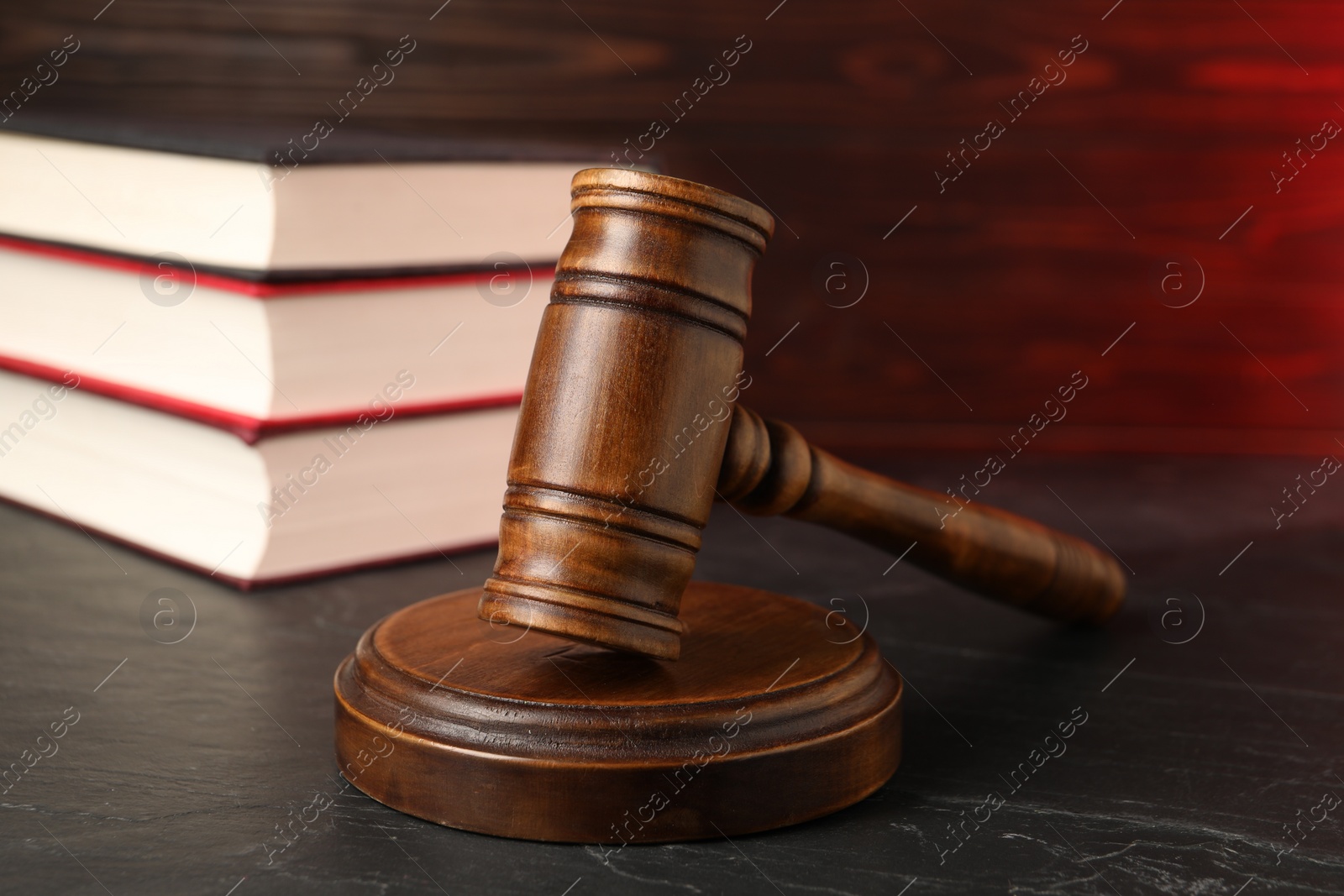 Photo of Wooden gavel and stack of books on dark textured table, closeup