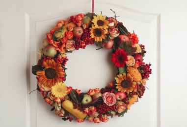 Photo of Beautiful autumnal wreath with flowers, berries and fruits hanging on white wooden door. Space for text