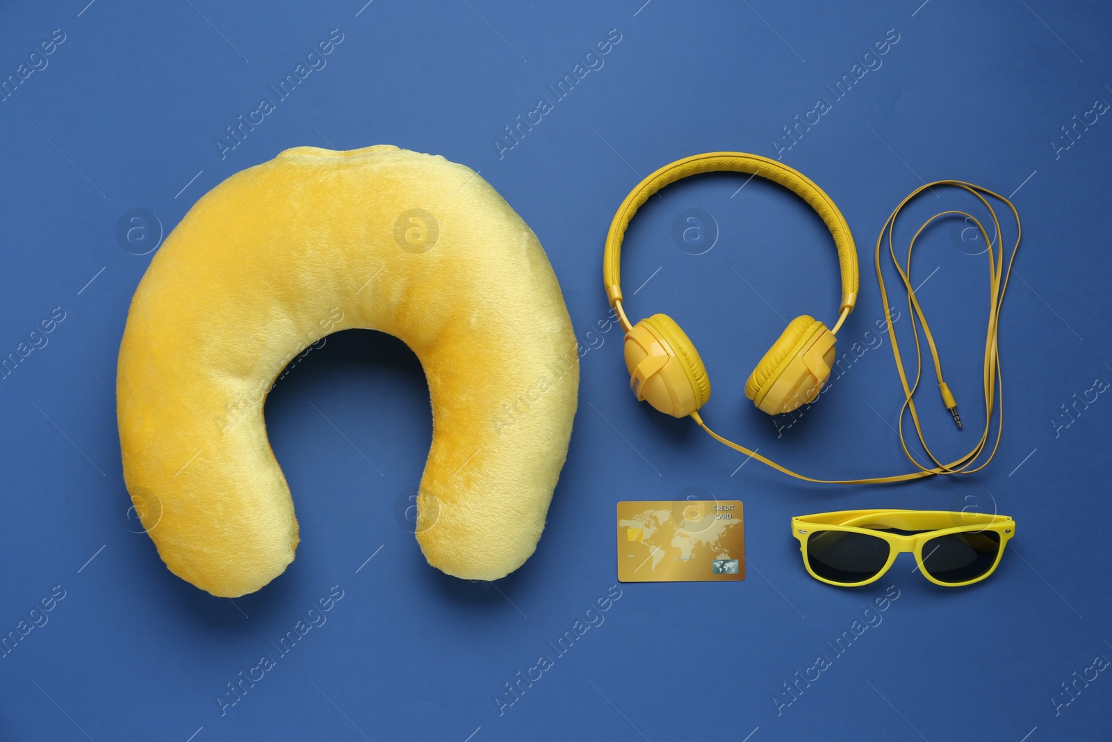 Photo of Yellow travel pillow, headphones, sunglasses and credit card on blue background, flat lay