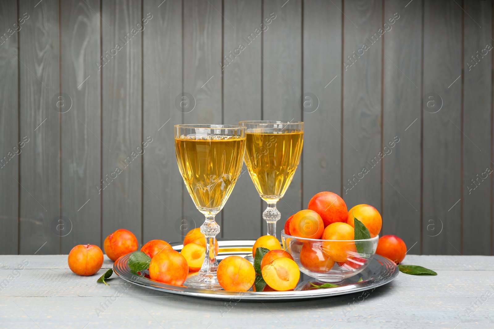 Photo of Delicious plum liquor and ripe fruits on table against grey background. Homemade strong alcoholic beverage