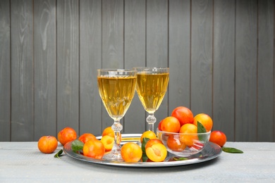 Photo of Delicious plum liquor and ripe fruits on table against grey background. Homemade strong alcoholic beverage