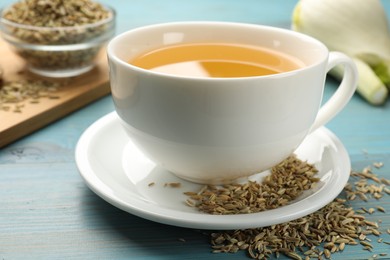 Photo of Fennel tea in cup, seeds and fresh vegetable on light blue wooden table, closeup