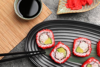 Photo of Delicious sushi rolls, soy sauce, ginger and chopsticks on grey textured table, flat lay