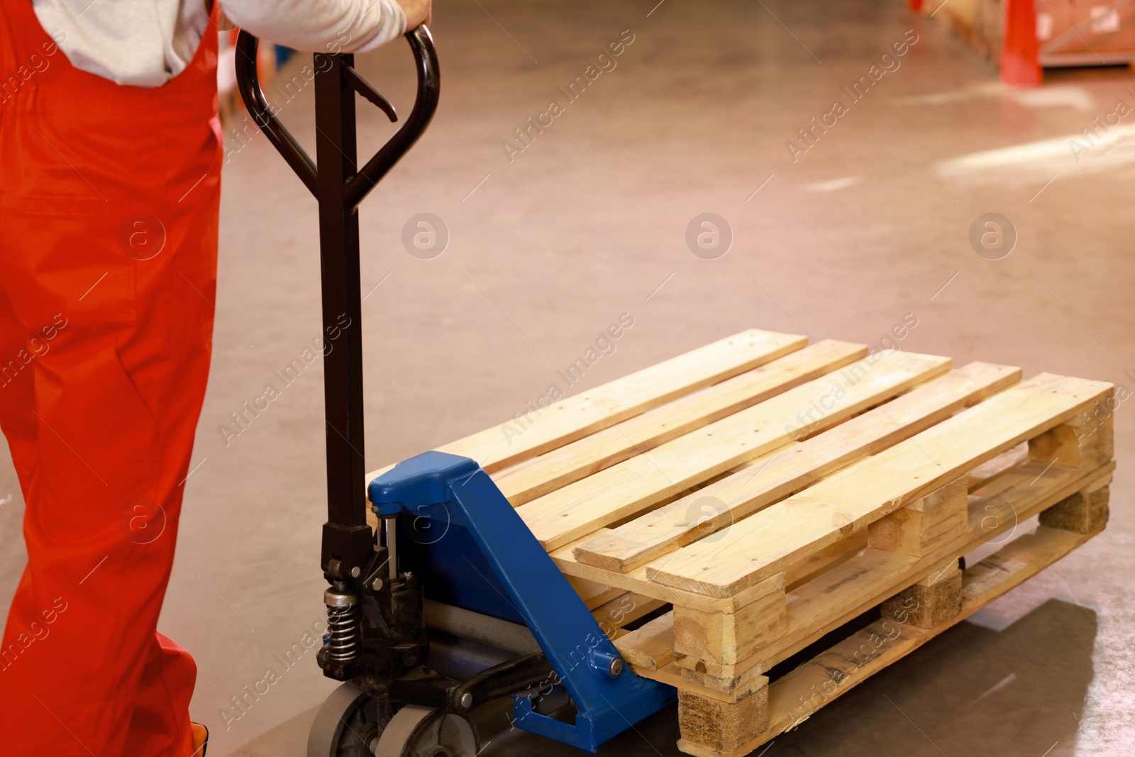 Image of Worker moving wooden pallets with manual forklift in warehouse, closeup