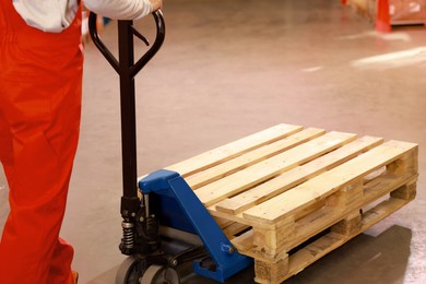 Image of Worker moving wooden pallets with manual forklift in warehouse, closeup