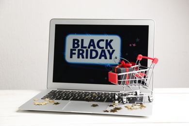 Photo of Laptop and small cart on white table. Black Friday Sale online