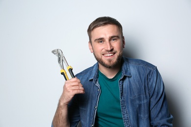 Photo of Young working man with adjustable pliers on light background