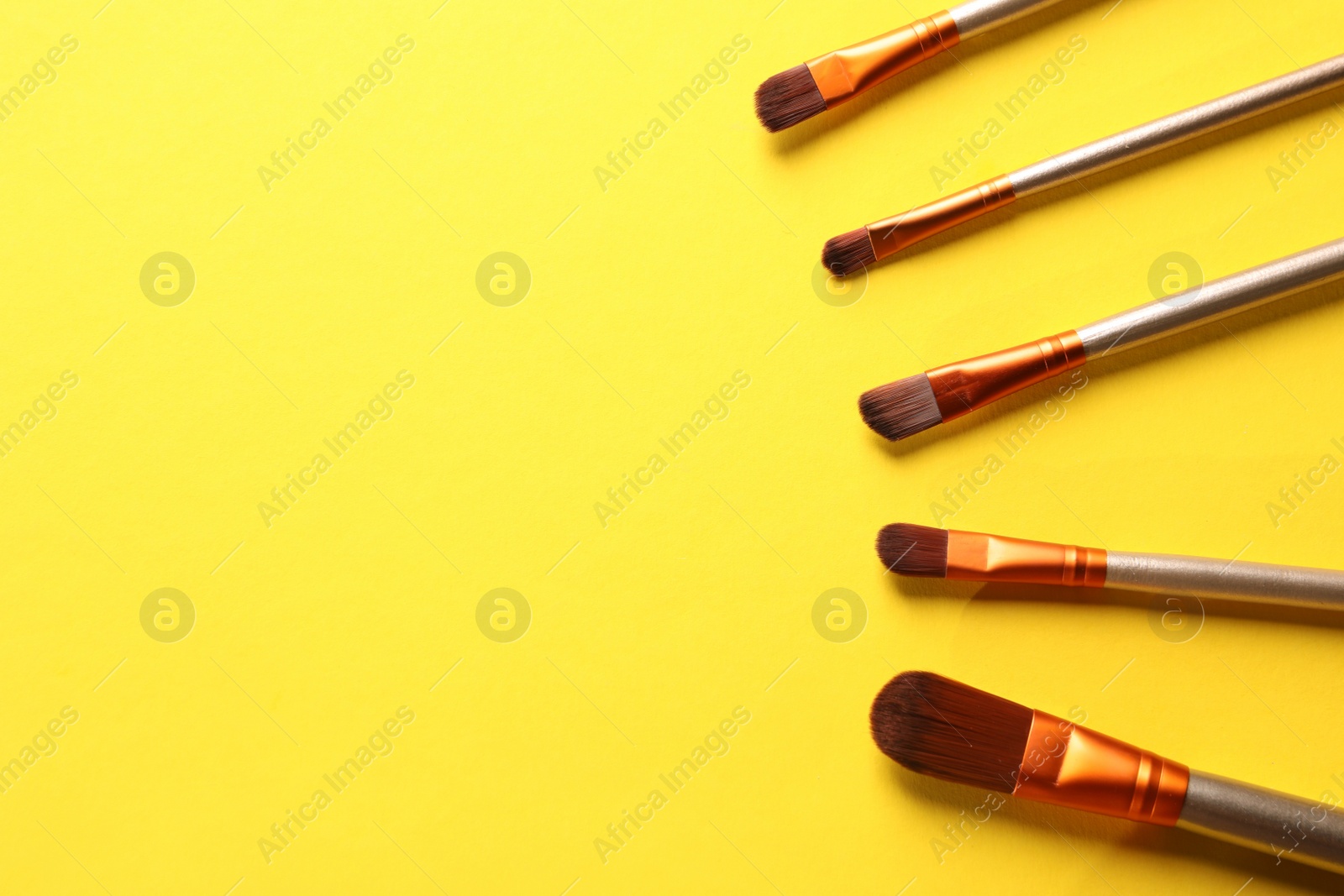 Photo of Different makeup brushes on yellow background, flat lay. Space for text