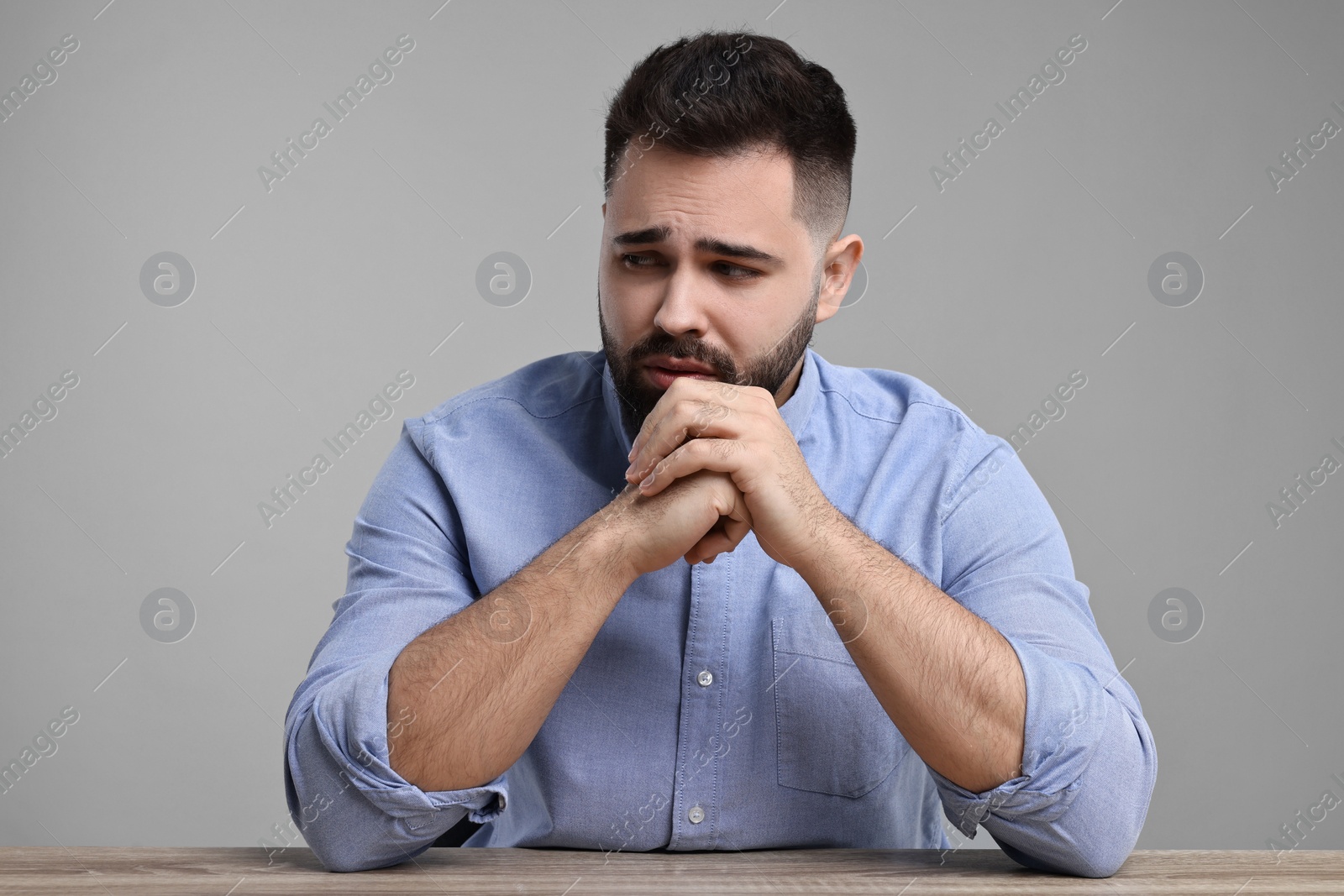 Photo of Portrait of sad man at wooden table on light grey background
