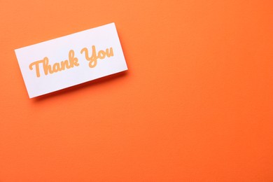 Photo of Note with phrase Thank You on orange background, top view. Space for text