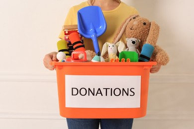 Photo of Woman holding donation box with toys against light background, closeup