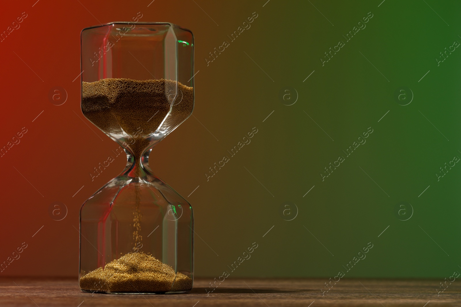 Photo of Hourglass with flowing sand on wooden table against color background, space for text