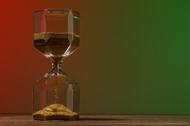 Photo of Hourglass with flowing sand on wooden table against color background, space for text