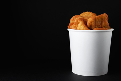 Photo of Bucket with delicious chicken nuggets on black background. Space for text