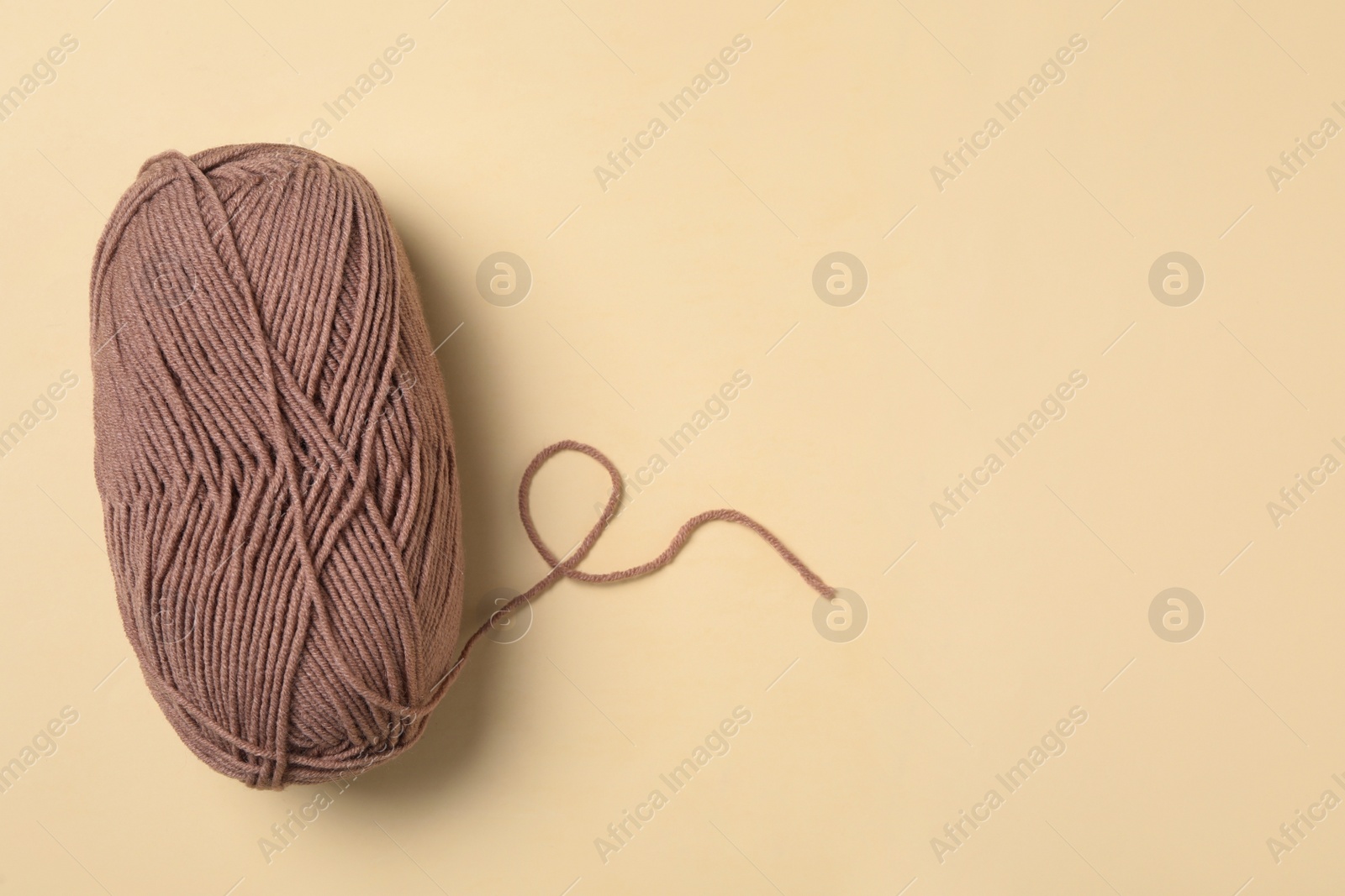 Photo of Soft brown woolen yarn on beige background, top view. Space for text