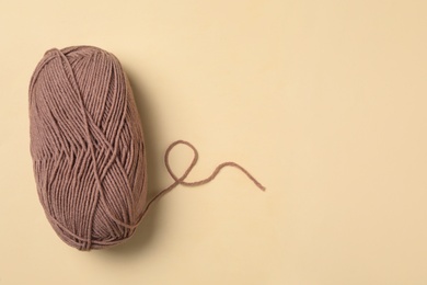 Photo of Soft brown woolen yarn on beige background, top view. Space for text