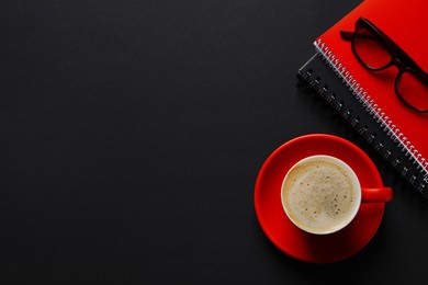 Photo of Red cup with aromatic cappuccino, notepads and glasses on black background, flat lay. Space for text