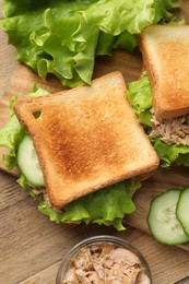 Photo of Delicious sandwiches with tuna, cucumber and lettuce leaves on wooden table, flat lay