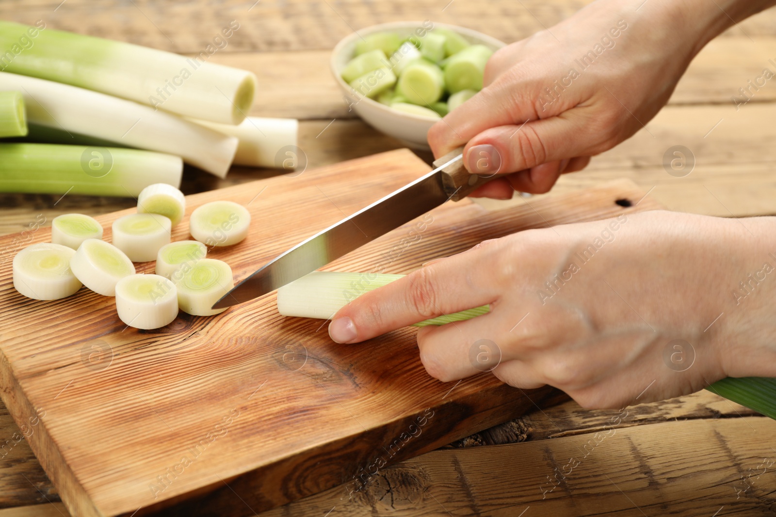 Photo of Woman cutting leek at wooden table, closeup