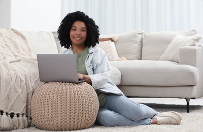 Happy young woman using laptop on pouf at home