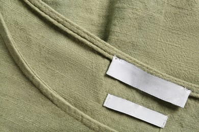 Photo of Blank clothing label on green apparel, top view. Space for text