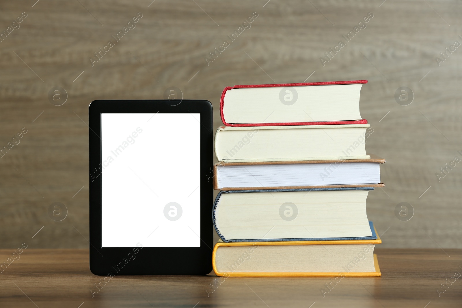 Photo of Portable e-book reader and stack of hardcover books on wooden table