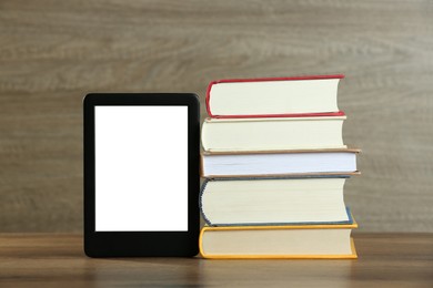 Portable e-book reader and stack of hardcover books on wooden table