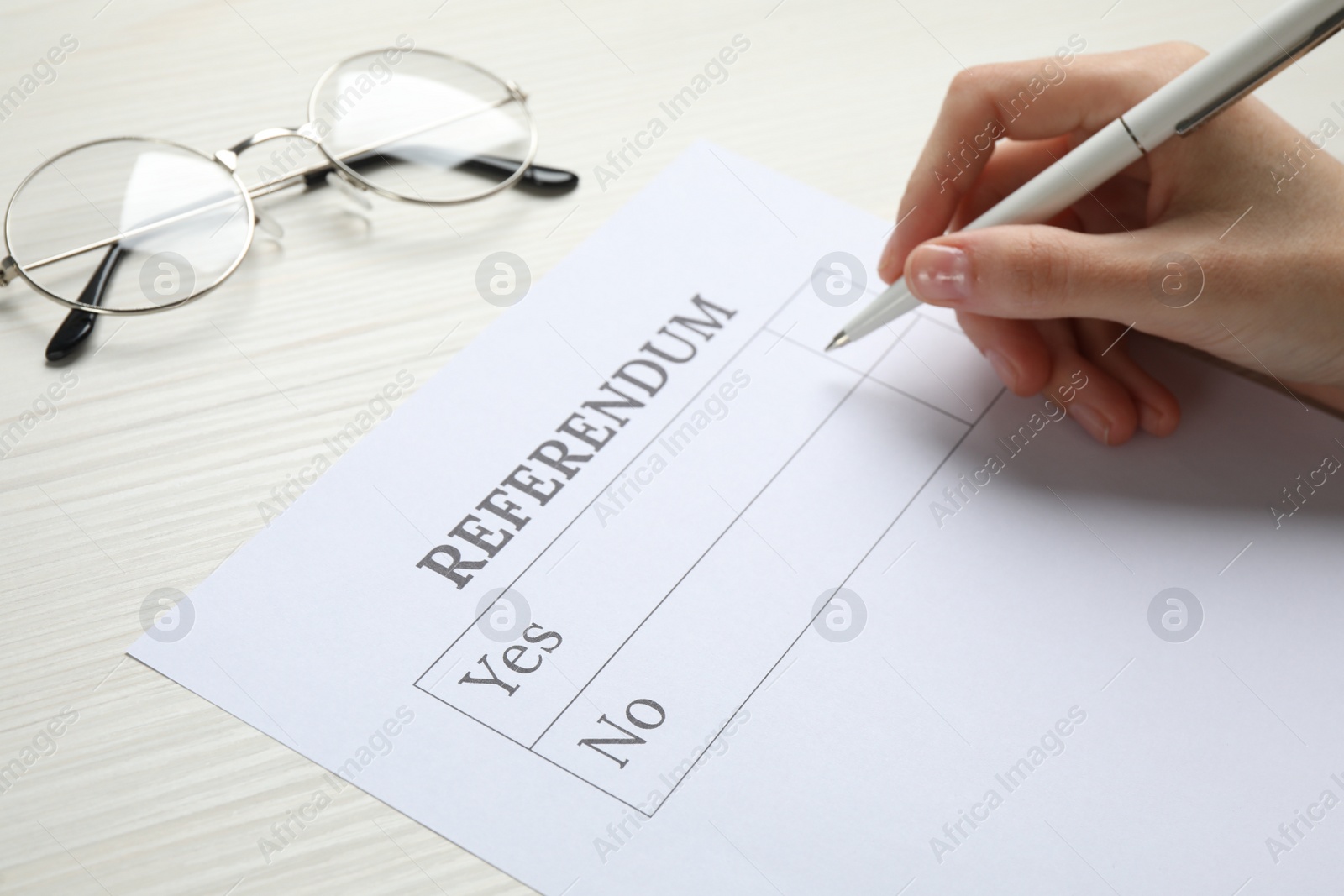 Photo of Woman with referendum ballot making decision at white wooden table, closeup