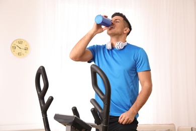 Man drinking water on modern elliptical machine at home