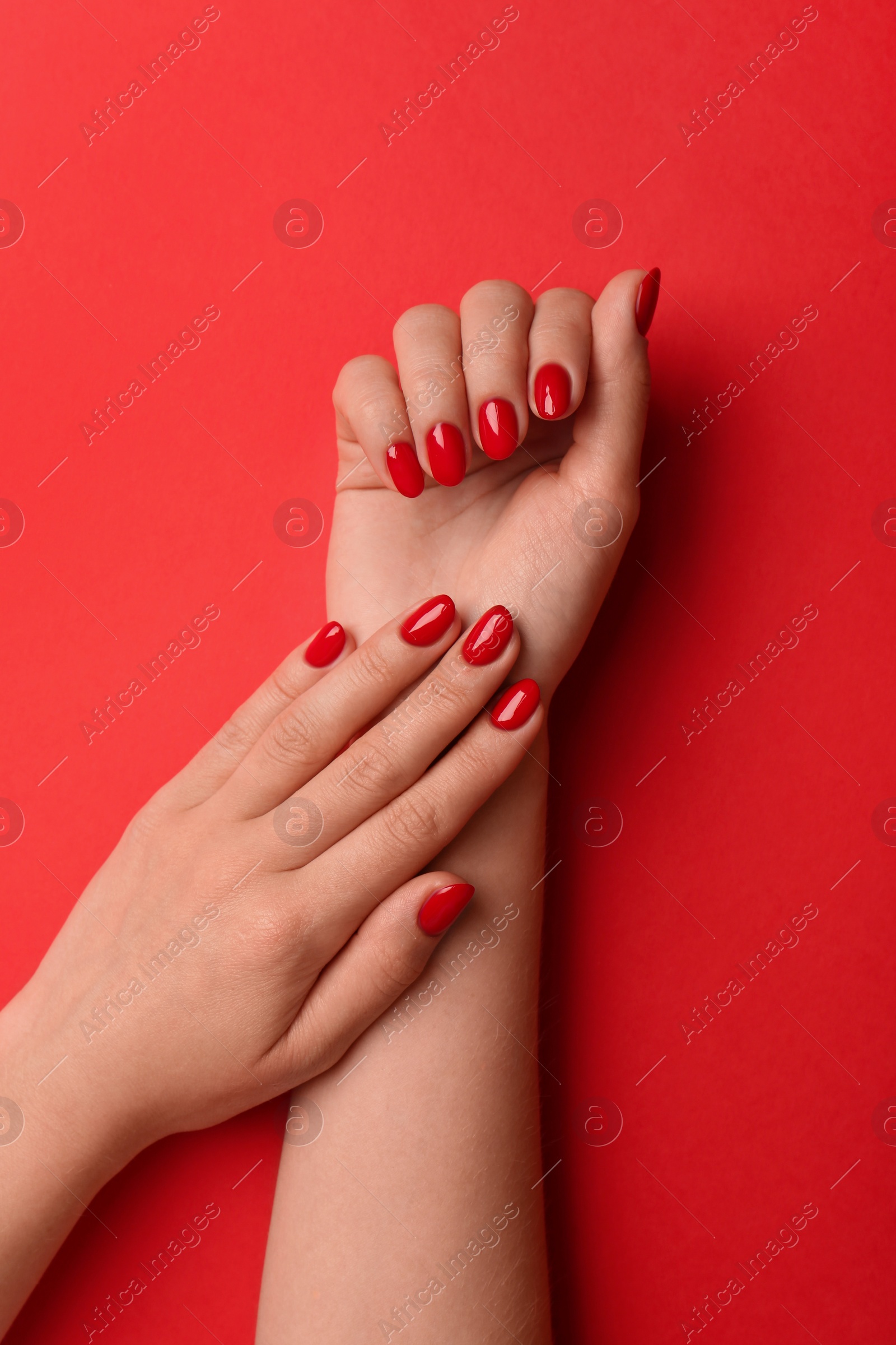 Photo of Woman with gel polish on nails against red background, top view