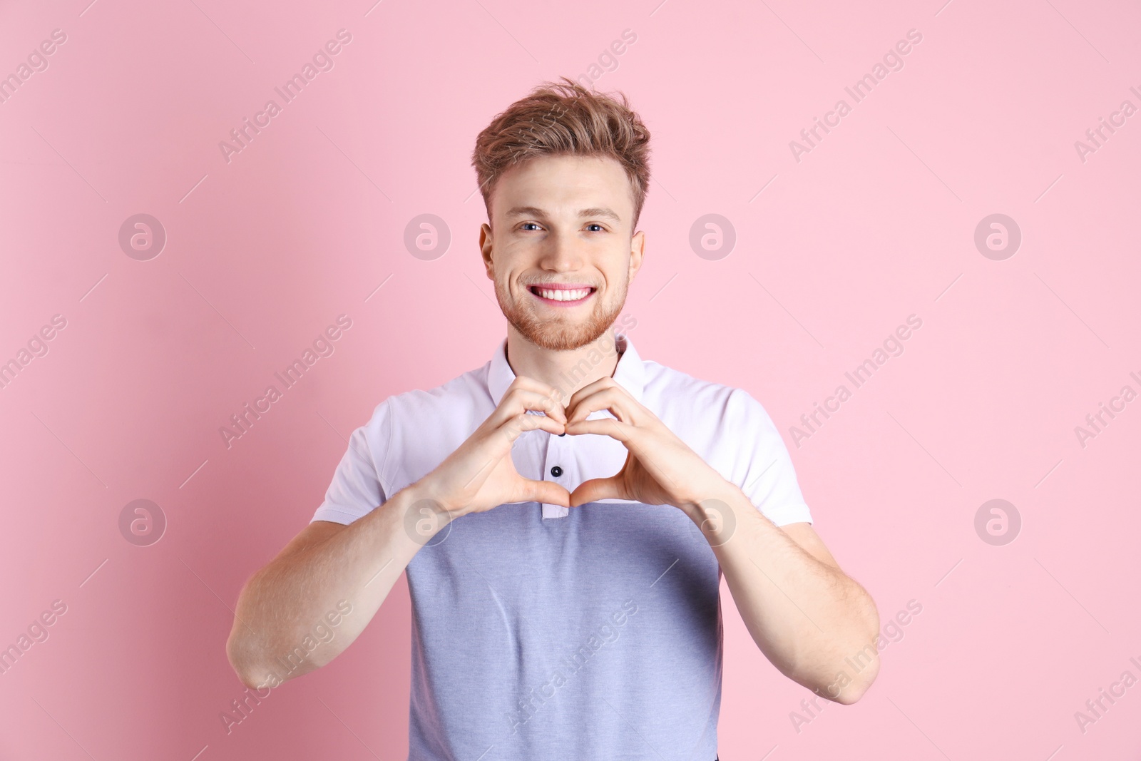 Photo of Portrait of young man making heart with his hands on color background