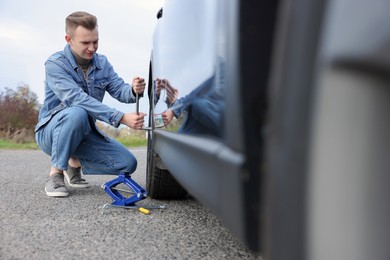 Young man changing tire of car on roadside