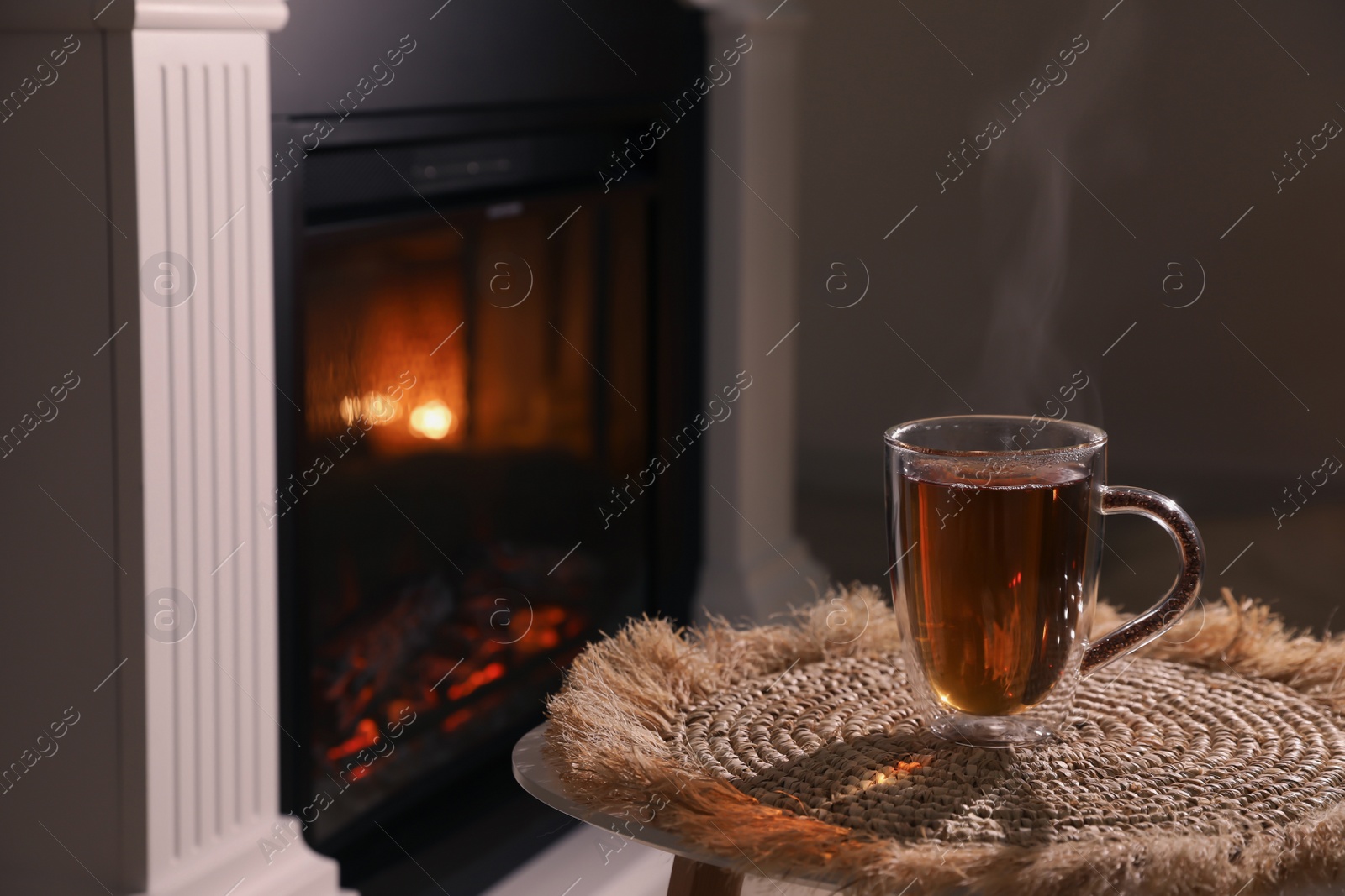 Photo of Glass of hot drink near fireplace in room. Space for text