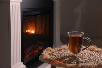 Photo of Glass of hot drink near fireplace in room. Space for text