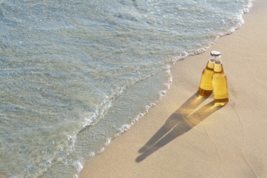 Photo of Bottles of cold beer on sandy beach near sea, space for text