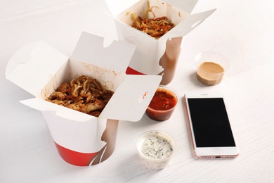 Photo of Mobile phone, Chinese noodles and different sauces on white table, space for text. Food delivery