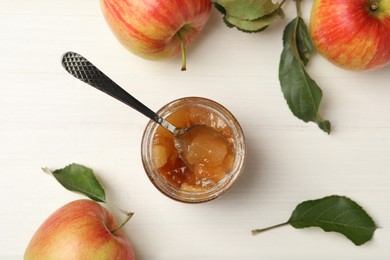 Photo of Tasty apple jam in glass jar and fresh fruits on white wooden table, flat lay